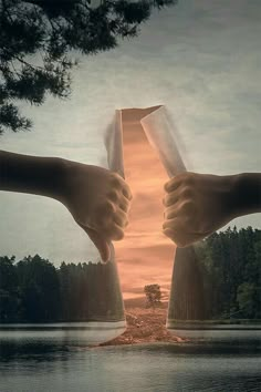 two hands holding papers over water with trees in the background