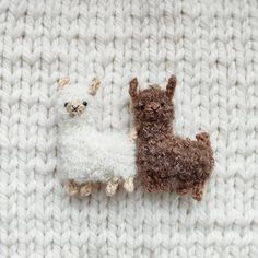 two stuffed llamas are laying on a white crocheted blanket, one is brown and the other is white