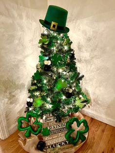 a small green christmas tree decorated with shamrocks, hats and bows on top is sitting in front of a white wall