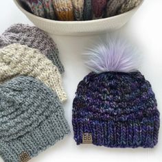 a knitted beanie with a purple pom - pom sits next to a bowl of yarn