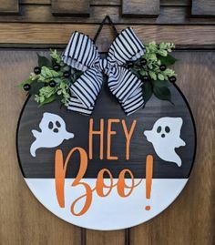 a sign that says hey boo on it with two ghost heads and green leaves hanging from the front door