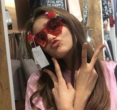 a woman wearing red sunglasses making the peace sign with her hand while standing in front of a store display