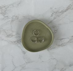 two wedding rings sitting in a green bowl on a marble counter top with white background