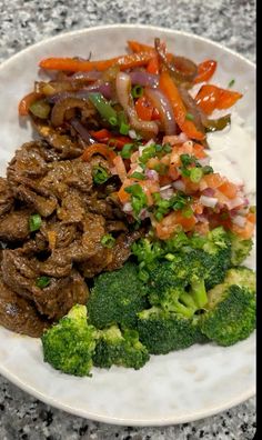 a white plate topped with meat and veggies on top of a granite counter