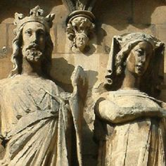 two statues of men and women in front of a stone wall with carvings on it