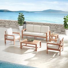 an outdoor living area with white furniture next to the pool and ocean in the background