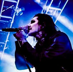 a man with long hair holding a microphone up to his mouth as he sings on stage