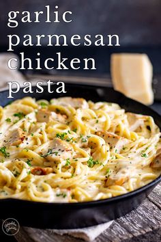 a skillet filled with pasta and chicken on top of a wooden table next to cheese