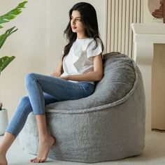 a woman sitting on a bean bag chair next to a plant in a living room