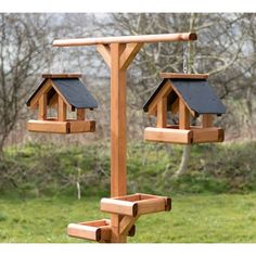 two wooden bird feeders hanging from the side of a pole in front of some trees