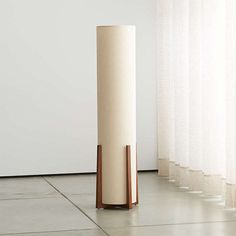 a tall white vase sitting on top of a floor next to a curtained window