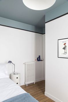 a bedroom with white walls and wood flooring has a painting on the wall next to the bed