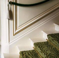 the stairs are lined with green carpet and gold trimmings, along with white walls