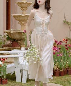 a mannequin wearing a white dress and holding a flower bouquet in front of a fountain