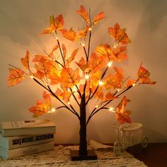 a lighted tree is sitting on a table next to some books and a glass vase