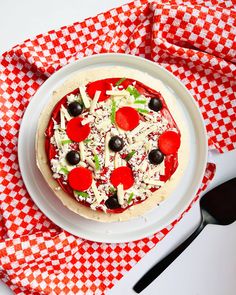 a pizza with olives, cheese and pepperoni on a red and white checkered napkin