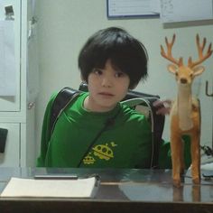 a young boy sitting in front of a desk with a deer toy next to him