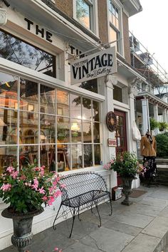 a store front with flowers in the window and an iron bench on the sidewalk outside