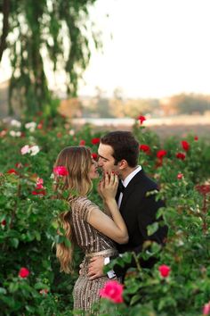 a man and woman are kissing in the middle of roses at their engagement photo shoot