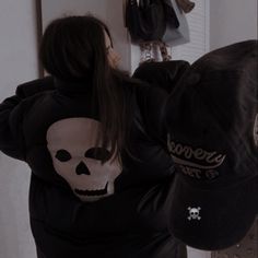 a person in a black jacket with a white skull on it's back and a hat hanging from the wall