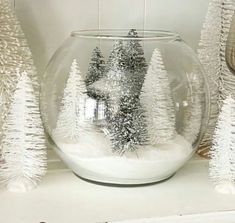 snow covered trees in a glass bowl sitting on a shelf next to other christmas decorations