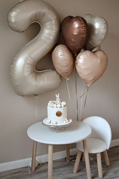 a table with a cake and balloons on it in front of a wall that says 2