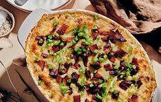 a baked dish with bacon, green onions and cheese on it next to other dishes