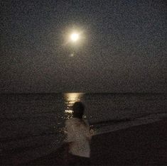 a person walking on the beach at night with the moon in the sky above them