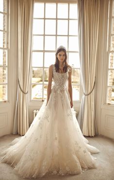 a woman standing in front of a window wearing a wedding dress