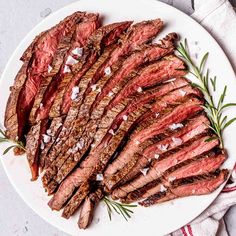 sliced steak on a white plate with rosemary garnish and salt sprinkled on top