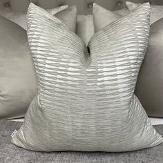 two silver pillows sitting on top of a bed next to a pillow case and headboard