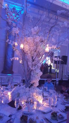 a tall vase filled with white flowers sitting on top of a table covered in plates and glasses