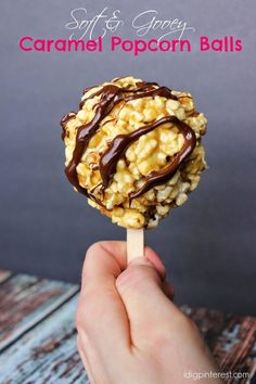 a hand holding a caramel popcorn ball on a stick with chocolate drizzle