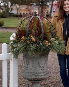 a woman standing next to a large potted planter with flowers and foliage in it