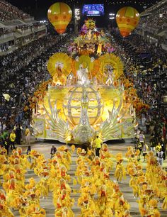 a large group of people dressed in yellow and orange dancing on a stage with balloons