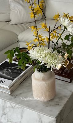 a marble table with flowers and books on it in front of a white couch,