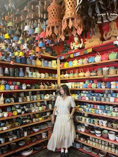 a woman is standing in front of shelves full of bowls and other items that are stacked on top of each other