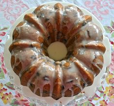 a bundt cake with icing on a glass plate and floral table cloth behind it