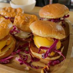 three burgers with cheese and onions on a wooden tray