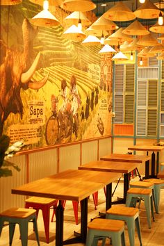 an empty restaurant with wooden tables and chairs in front of a large mural on the wall