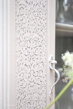 a close up of a door handle on a white door with flowers in the background