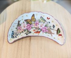 a decorative plate with flowers and butterflies on it sitting on top of a wooden table