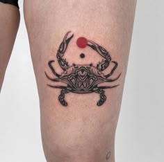 a black crab tattoo on the right thigh, with a red dot at the center