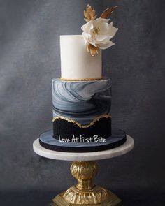 a three - tiered cake with white flowers on top sits on a gold pedestal