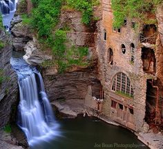 a waterfall in the middle of a cliff with a building on it's side