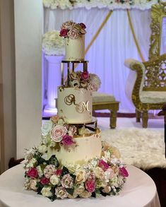 a three tiered wedding cake with pink and white flowers on the table in front of a chair