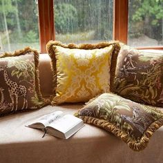 a couch with several pillows and a book on it next to a window sill