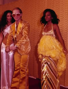 two women and a man dressed up in disco outfits posing for the camera with their arms around each other