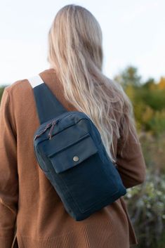 a woman with blonde hair is carrying a blue backpack in her hand and looking at the ground