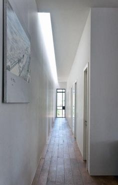 an empty hallway with white walls and tile flooring, leading to a large painting on the wall